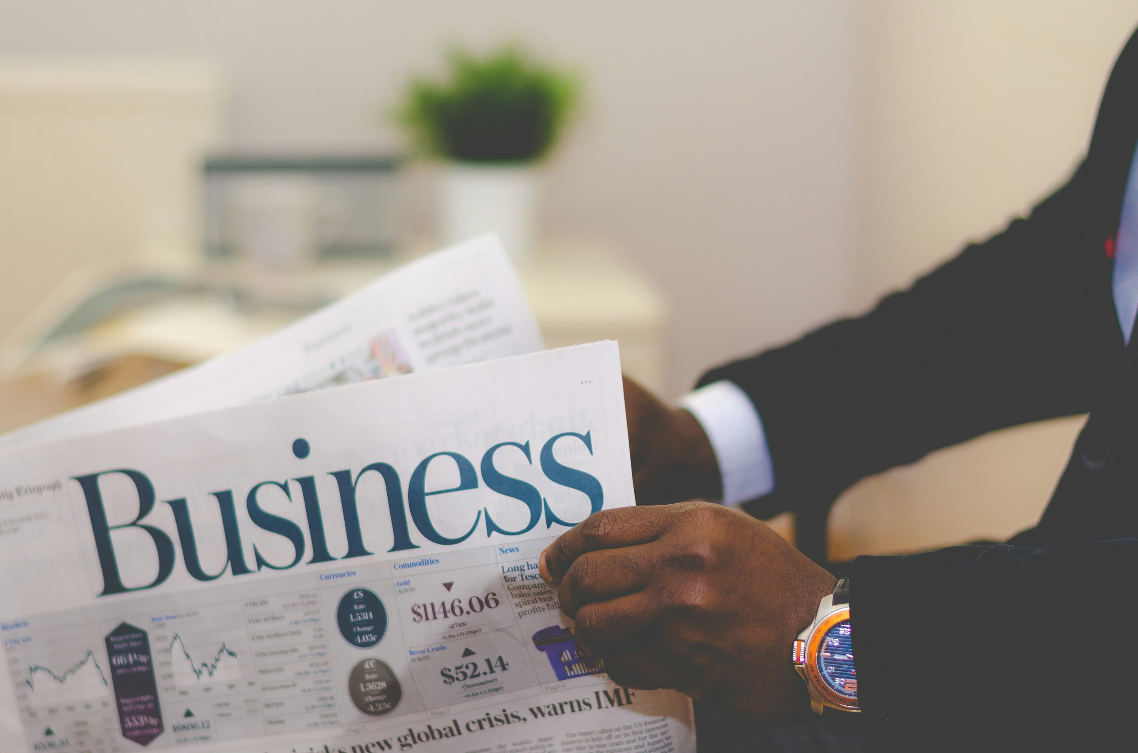Close-up of a businessman's hands holding a newspaper with a large 'Business' section headline.