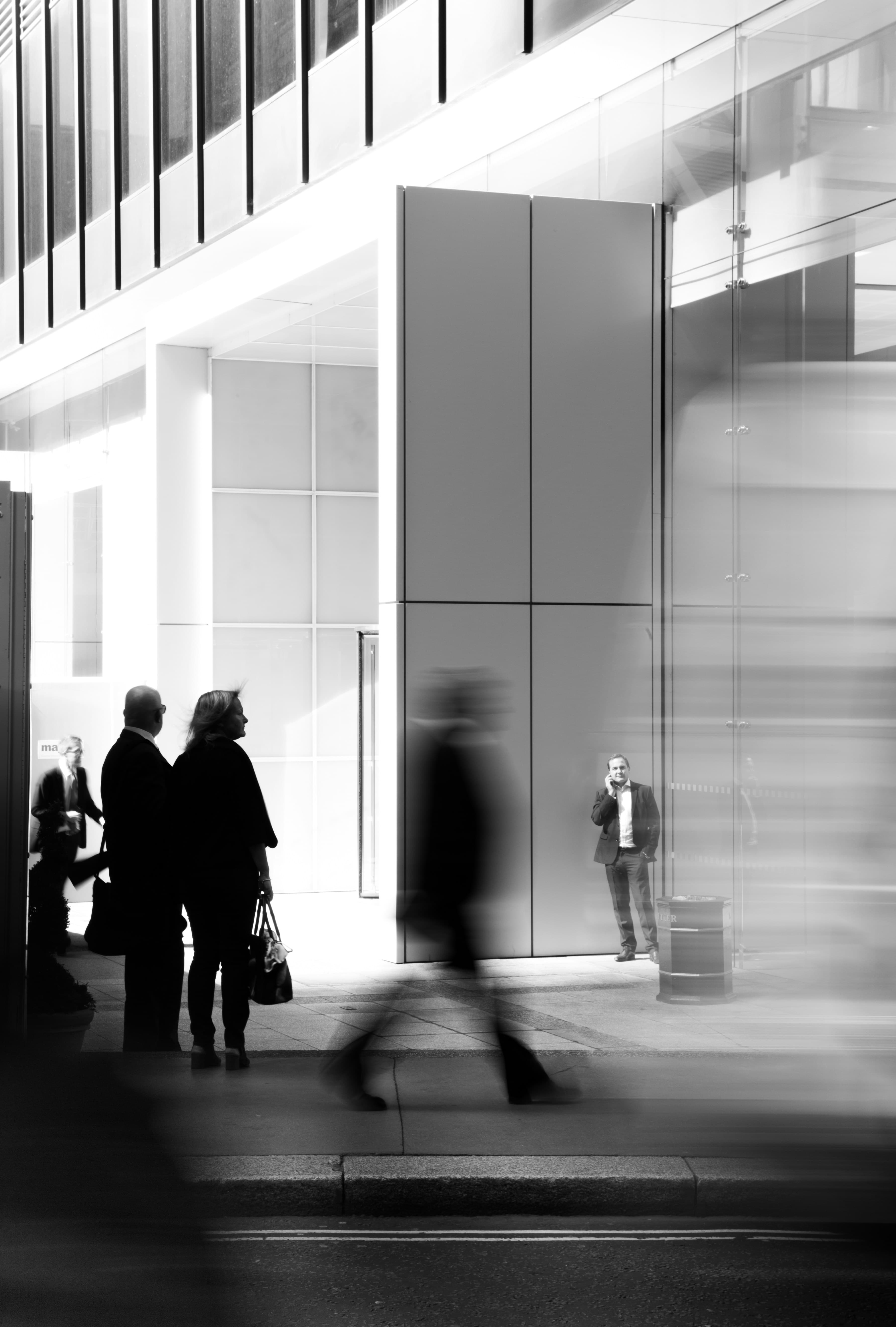 Black and white urban scene with motion-blurred pedestrians walking past a modern glass building.
