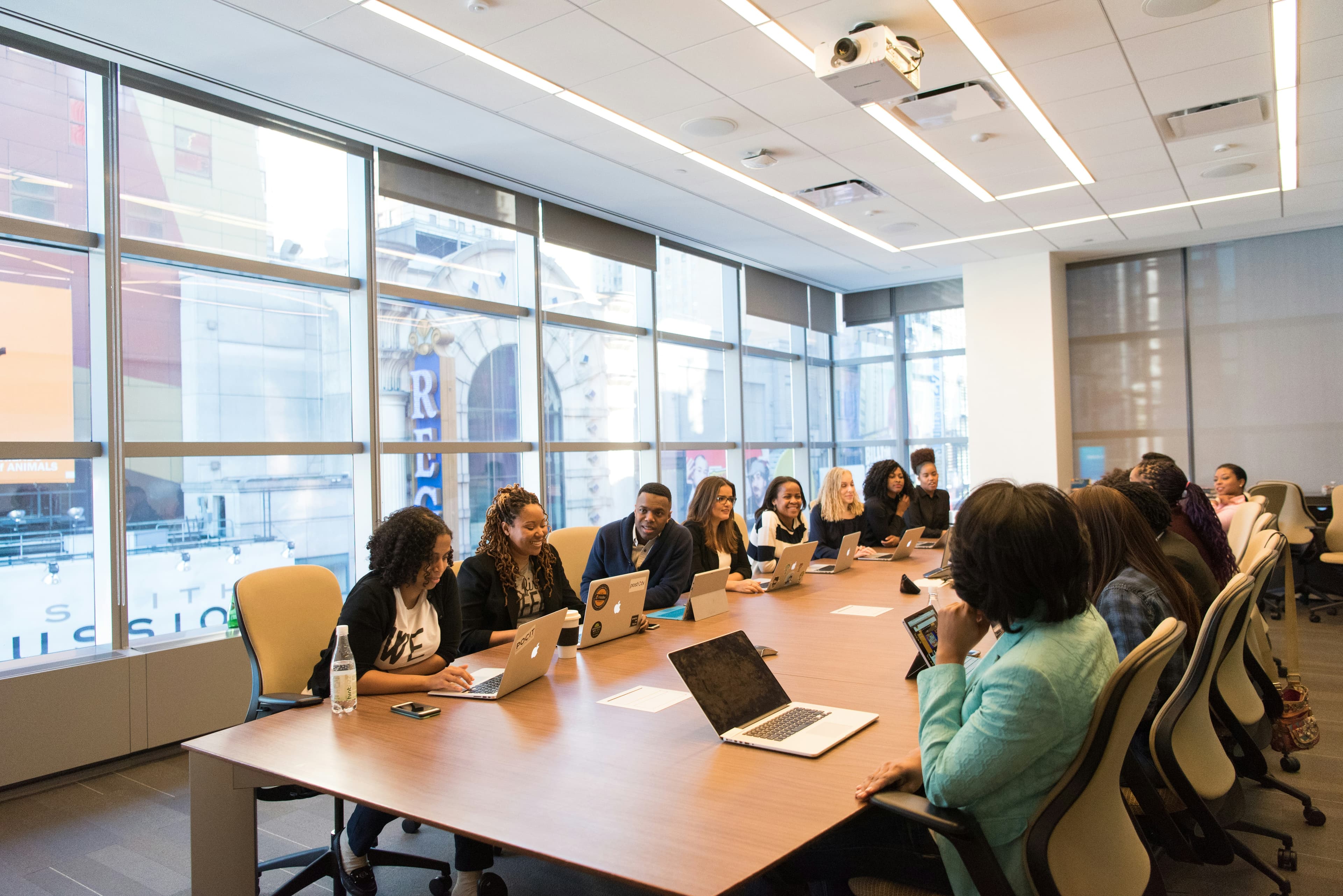 Diverse professionals using laptops around a long conference table in a bright modern office.