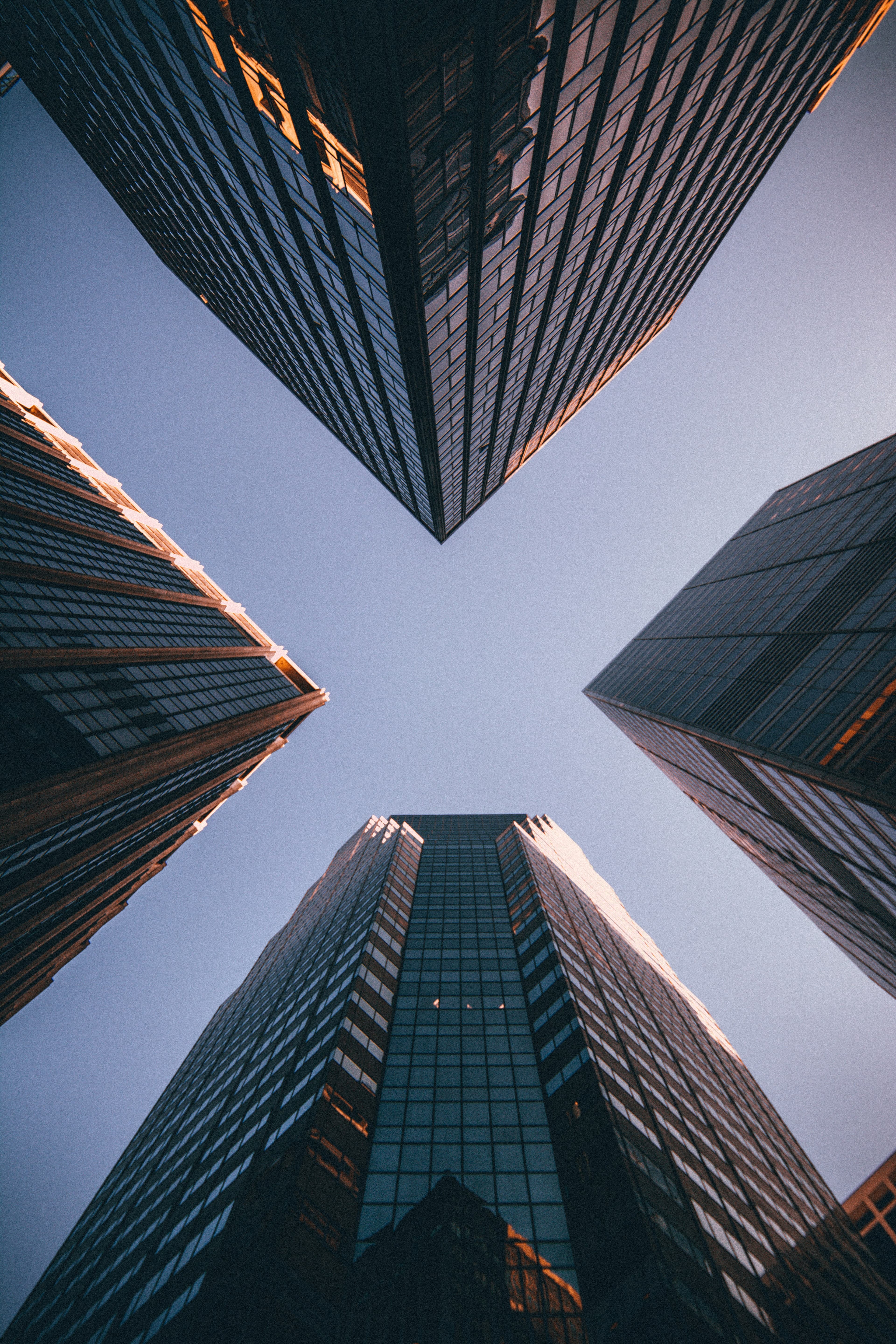 Low-angle view of four glass skyscrapers converging towards a clear sky in golden light.