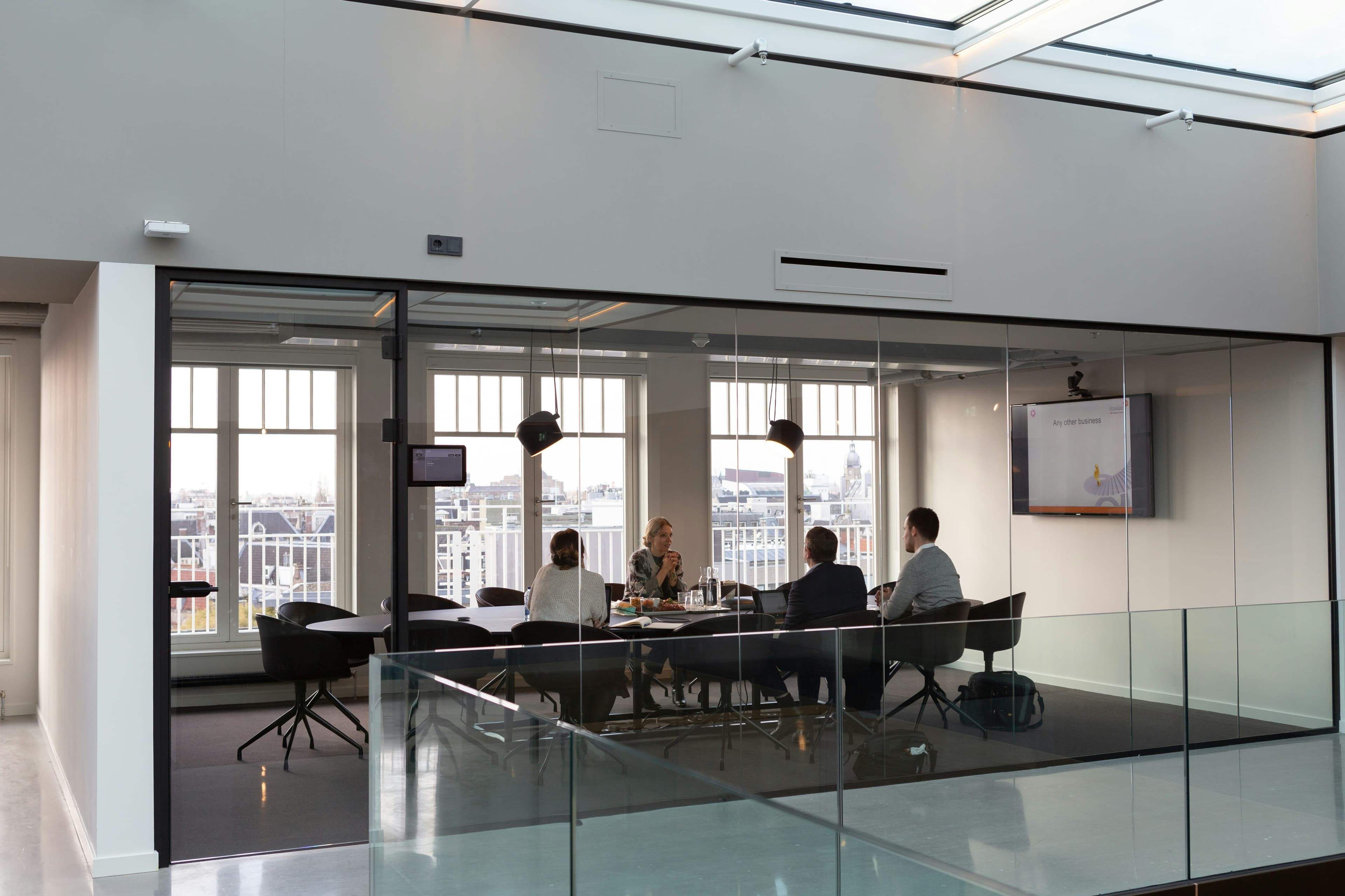 Four professionals meeting in a glass-walled conference room with a presentation screen and city view.